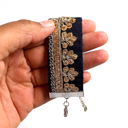 Hand holding a navy blue bracelet with gold embroidered design on a plain background.