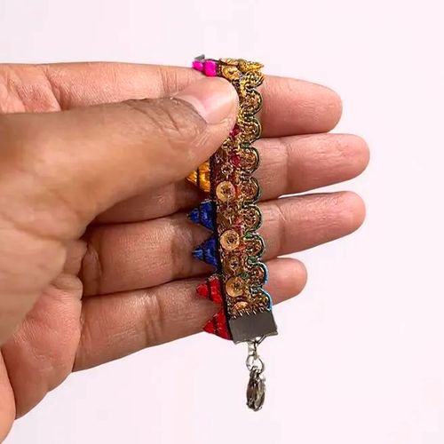 Hand holding a colourful bracelet with rainbow bunting and gold sequins on a plain background.