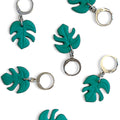 Collection of handmade green monstera leaf charms on silver huggie hoops with a white background.
