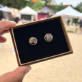 Handmade round ceramic stud earrings in a glossy iridescent lack colour in a gift box with luxury black velvet, held by a hand with a blurred outdoor background.