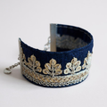 Navy blue bracelet with gold embroidered design on a plain background.