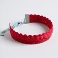 Red braided bracelet with a silver clasp on a plain background.